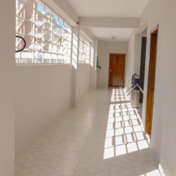 a foto mostra um dos corredores do IPC, com cho e paredes brancas. H janelas abertas  esquerda, ao alto.  direita, h portas em madeira marrom. Ao fundo, est uma porta marrom fechada.